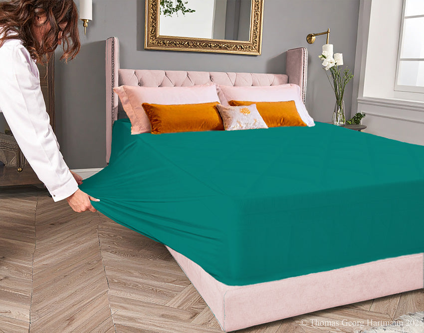 Evergreen jersey-knit stretch fitted sheet on an extra-deep mattress — pulling the sidewall over a foot outward to demonstrate the abundant stretch, making sheet changing effortless even for those with limited strength or mobility.