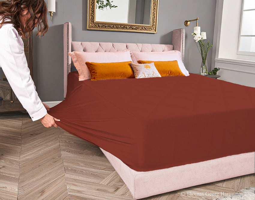 Redwood jersey-knit stretch fitted sheet on an extra-deep mattress — pulling the sidewall over a foot outward to demonstrate the abundant stretch, making sheet changing effortless even for those with limited strength or mobility.
