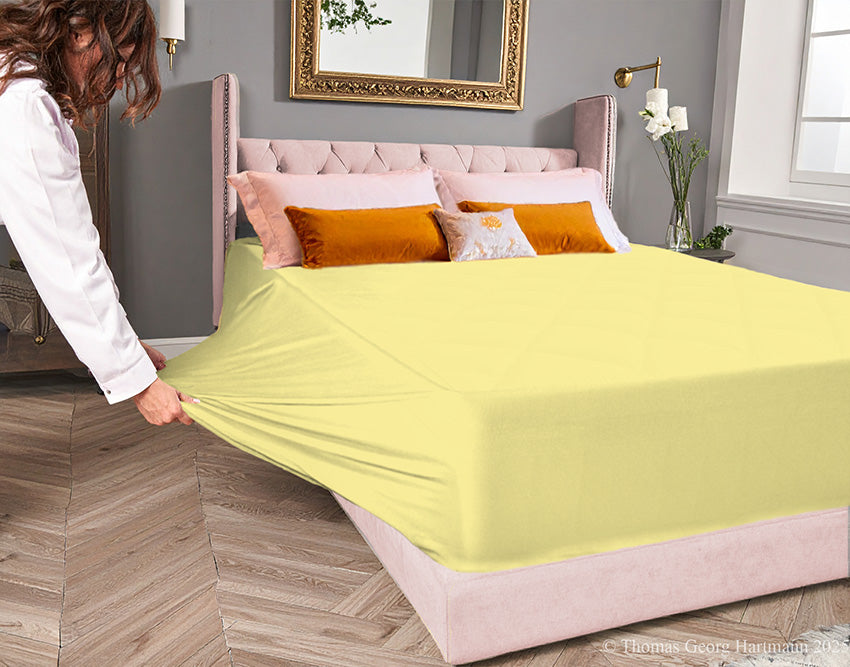 Sun jersey-knit stretch fitted sheet on an extra-deep mattress — pulling the sidewall over a foot outward to demonstrate the abundant stretch, making sheet changing effortless even for those with limited strength or mobility.
