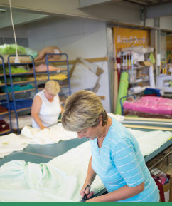 Two employees custom-tailoring our Jersey Knit Stretch sheets