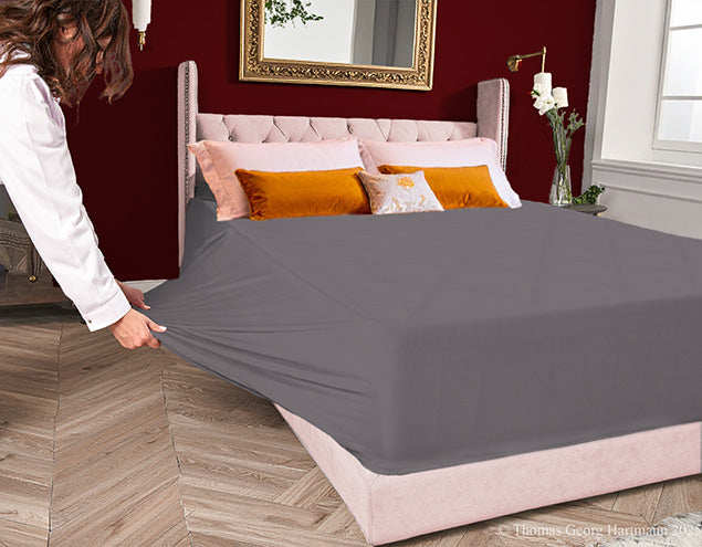 Pulling the stretch jersey knit fitted sheet over the extra deep Queen-size mattress for an easy, snug fit (graphite).