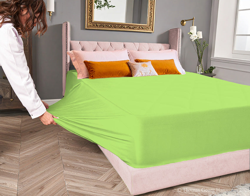 Green-apple jersey-knit stretch fitted sheet on an extra-deep mattress — pulling the sidewall over a foot outward to demonstrate the abundant stretch, making sheet changing effortless even for those with limited strength or mobility.