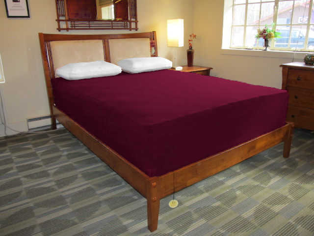 Bed with burgundy colored Jersey knit stretch sheet on extra-deep queen-size mattress.