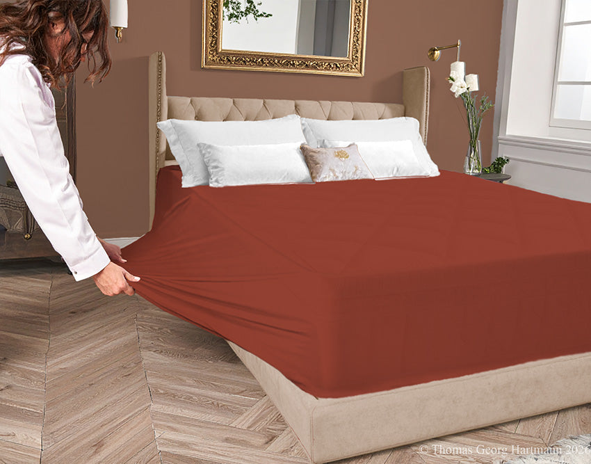 Redwood jersey-knit stretch fitted sheet on an extra-deep mattress — pulling the sidewall over a foot outward to demonstrate the abundant stretch, making sheet changing effortless even for those with limited strength or mobility.