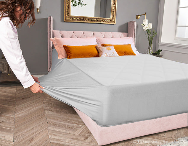 Pulling the stretch jersey knit fitted sheet over the  extra deep Queen-size mattress for an easy, snug fit (silver).