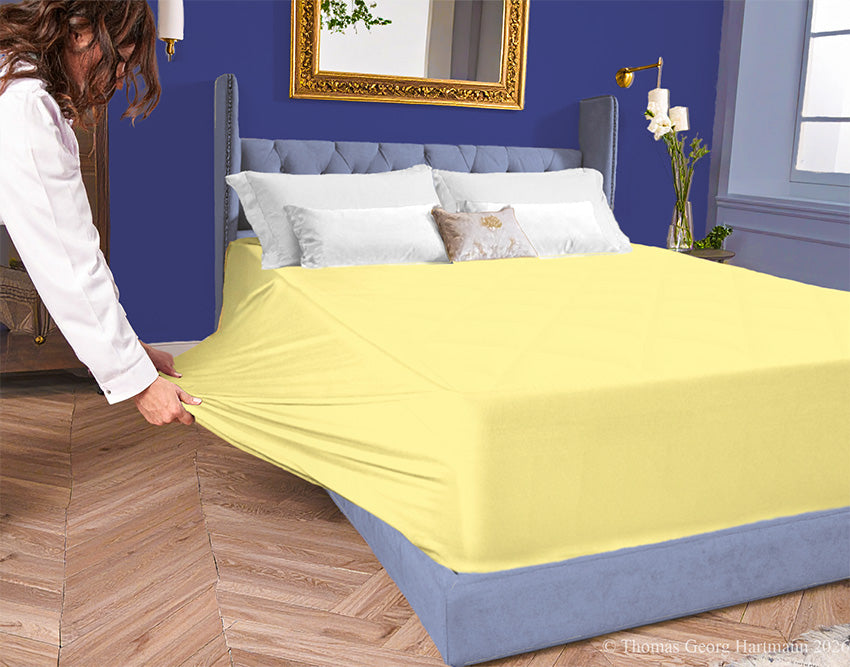 Sun jersey-knit stretch fitted sheet on an extra-deep mattress — pulling the sidewall over a foot outward to demonstrate the abundant stretch, making sheet changing effortless even for those with limited strength or mobility.